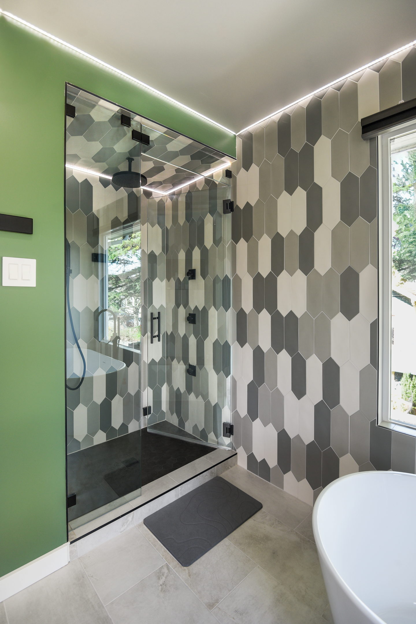 A walk-in shower tiled in elongated gray hexagons next to a freestanding tub