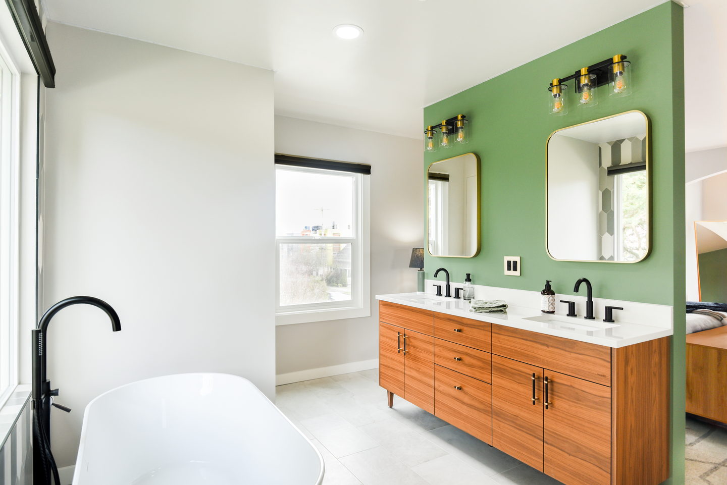 A freestanding white tub set beneath a window with gray patterned tile behind