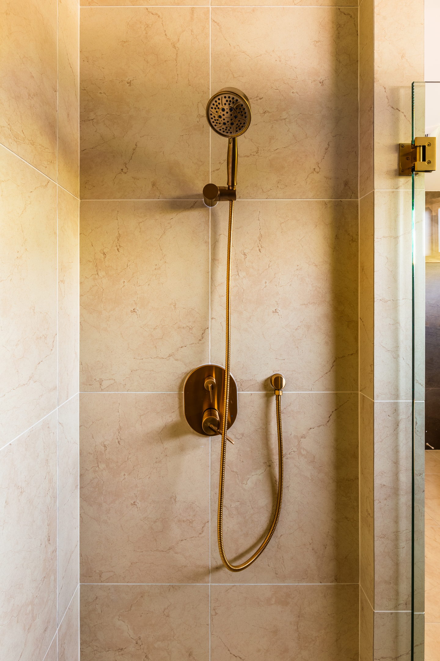 Close view of an unlacquered brass shower valve and handset on warm stone tile