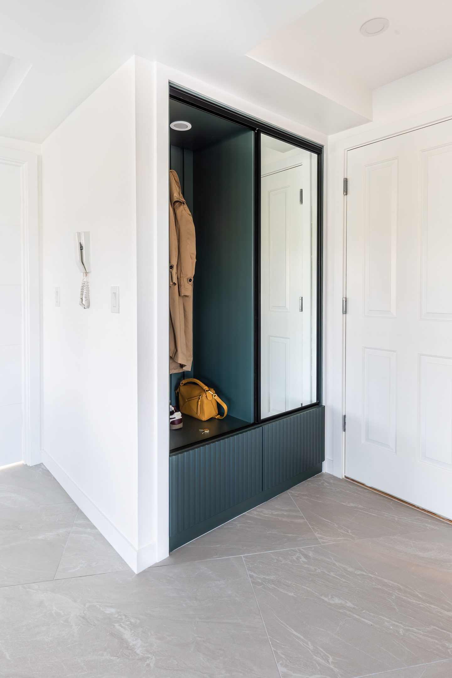 An entry lined in deep green panelled cabinetmaking with a full-height mirror