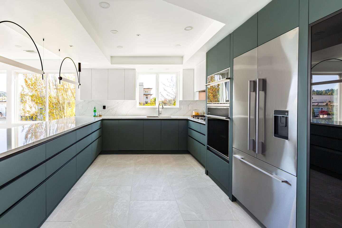 A Kirkland condo kitchen in matte deep green with arched pendant lights and a marble backsplash
