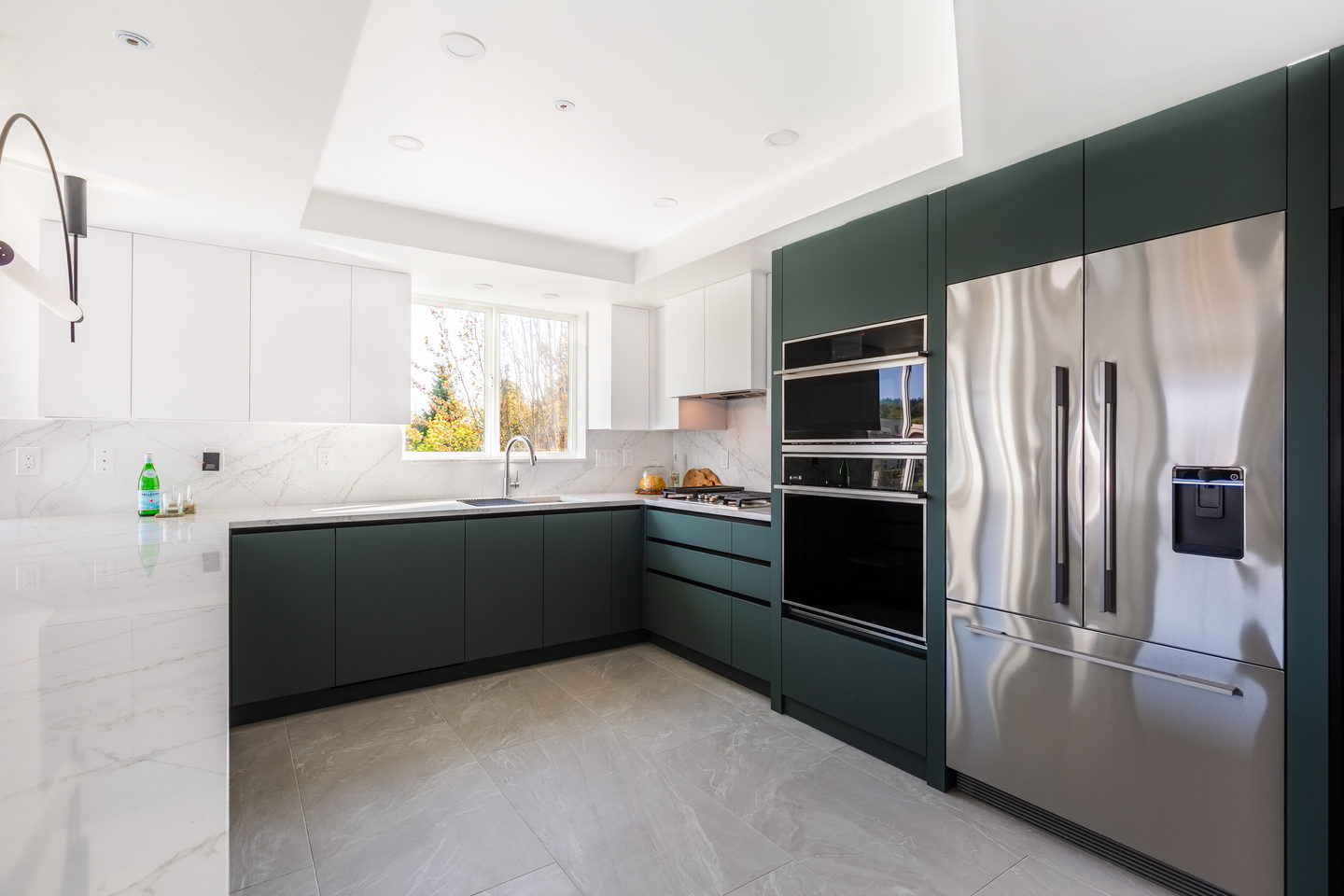 The green kitchen seen from the living room, with integrated ovens and a tall fridge