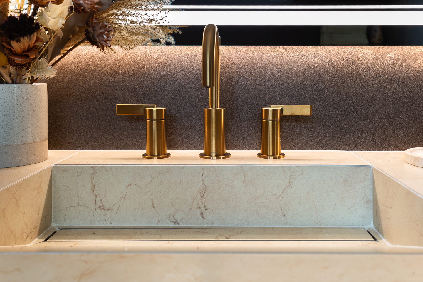 A stone sink surround with a gold bridge faucet in the primary bathroom
