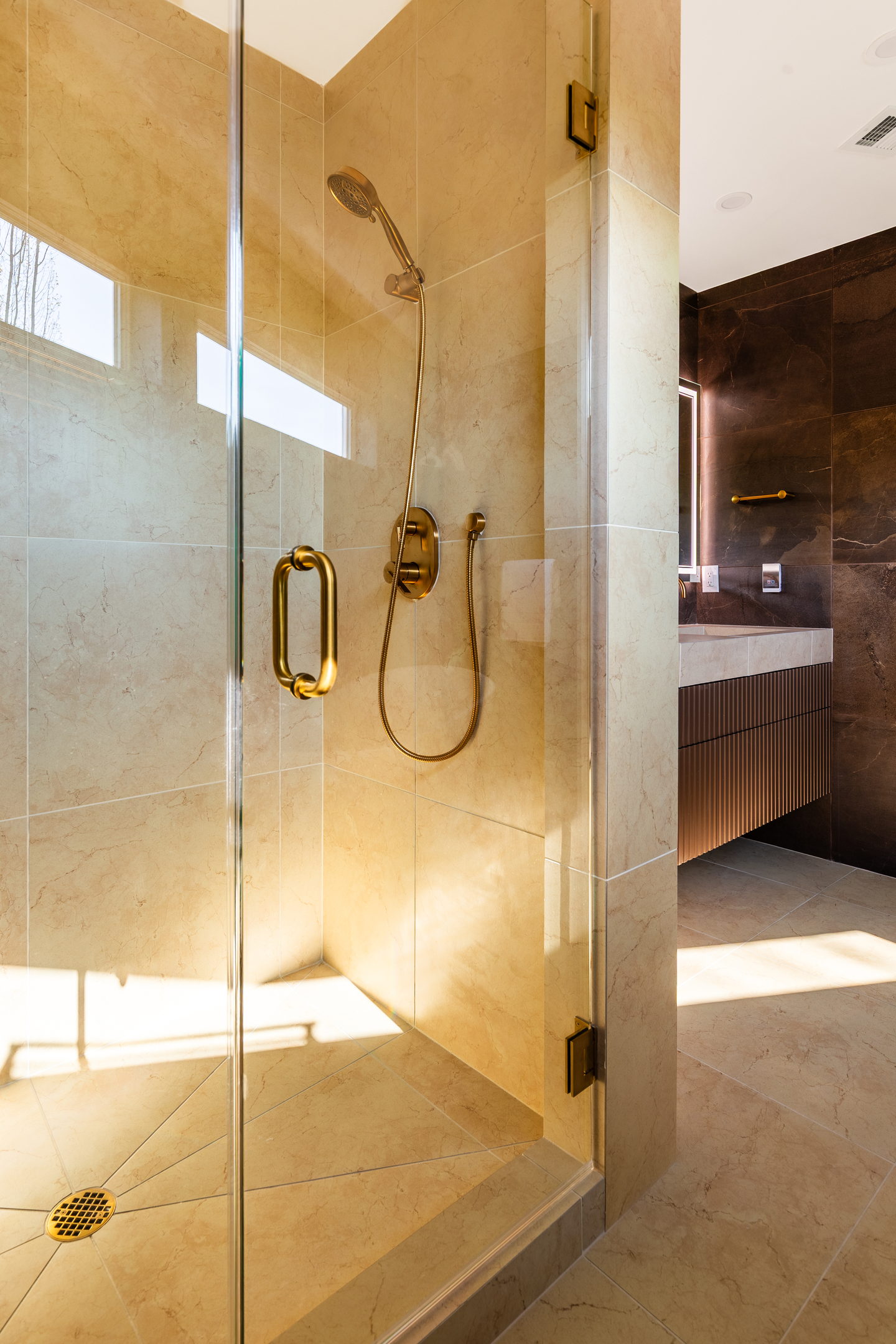 The warm stone shower with brass fittings and a frameless glass door