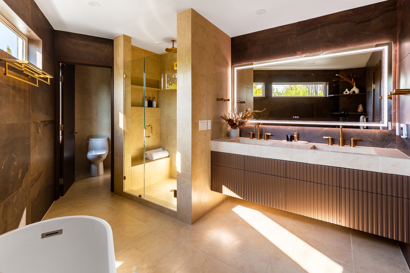 The primary bath with a backlit mirror, fluted vanity and the tub beyond