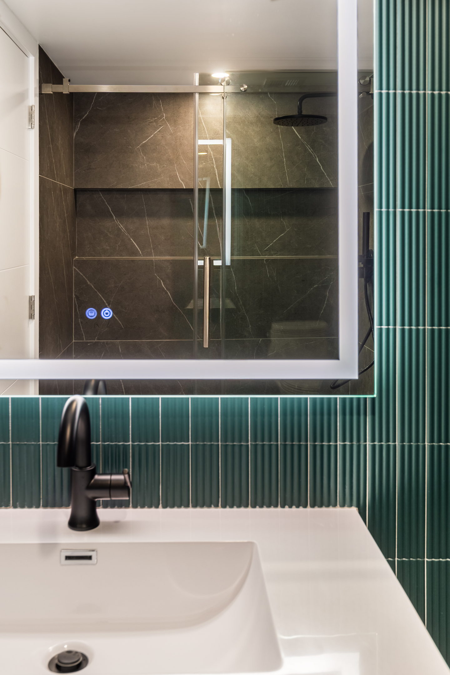 The guest bath in vertical green tile with a black faucet and a white sink