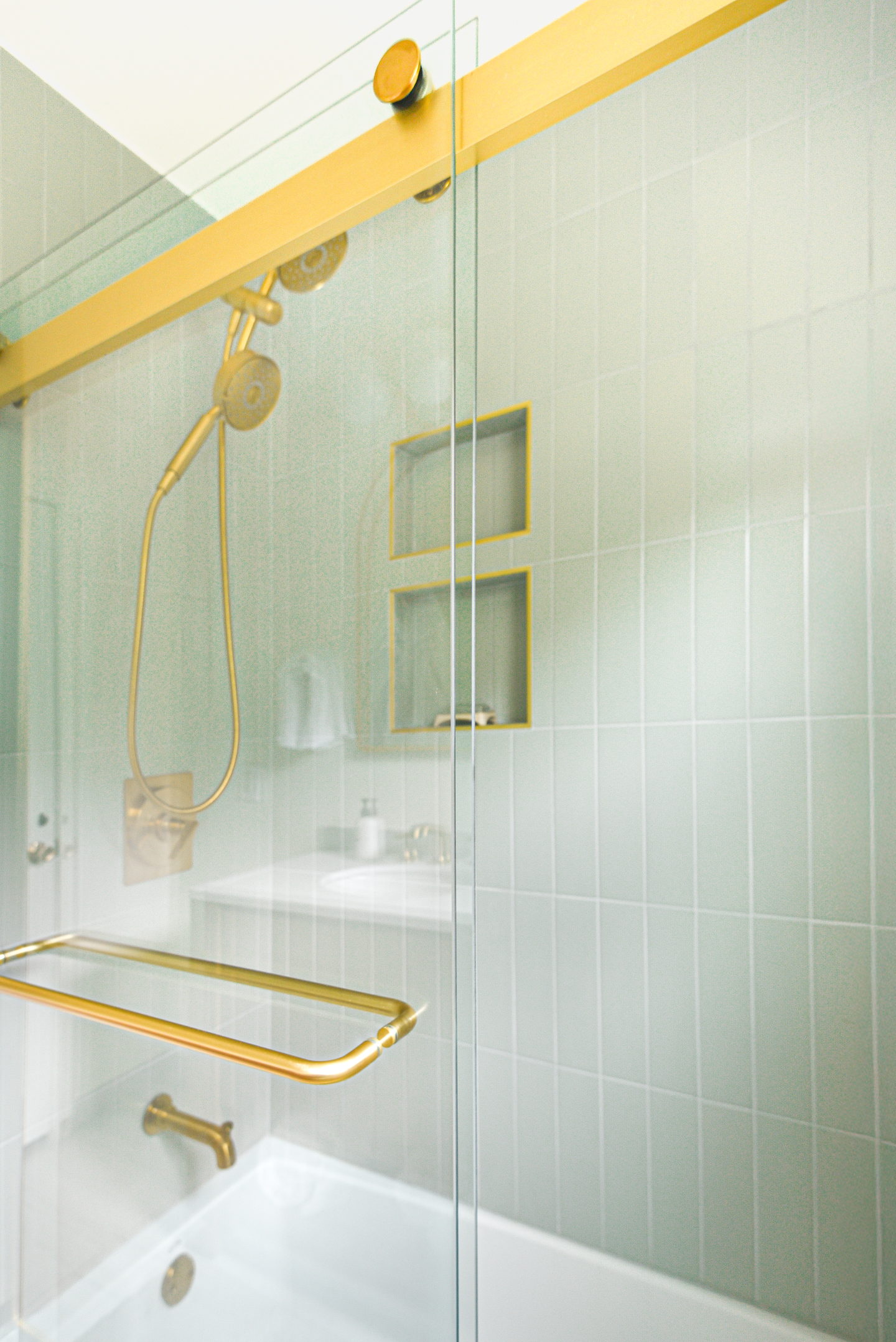 A shower in pale green stacked tile with brass fittings and a glass screen