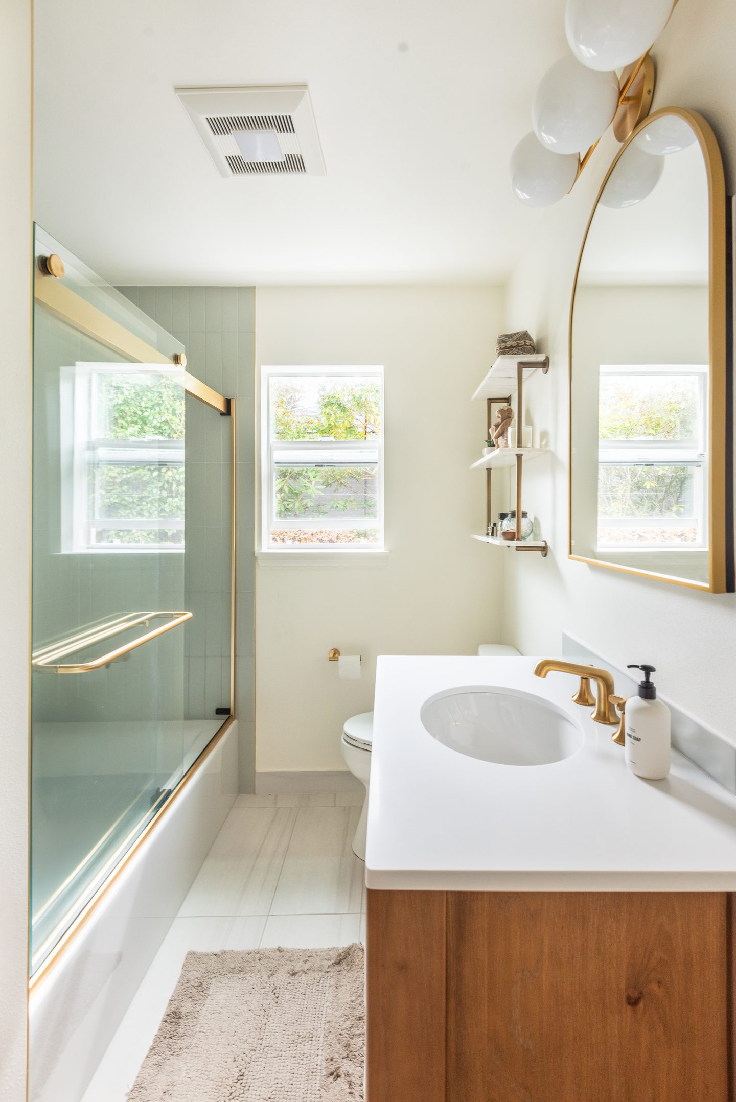 The bath and shower with an arched mirror and walnut vanity beyond