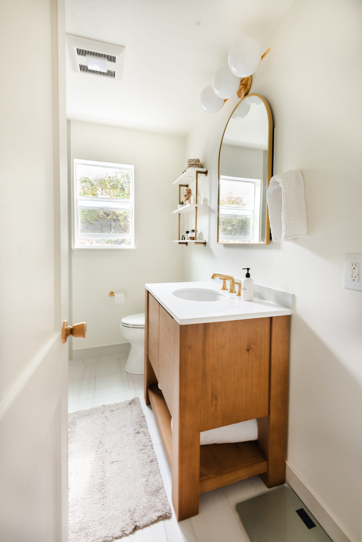 A walnut vanity with a white sink and an arched mirror in a bright bathroom