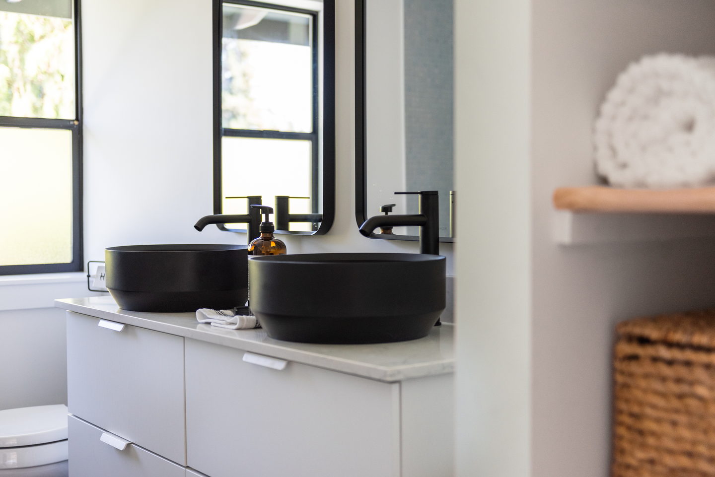 A black stone sink on a white counter with a black faucet and a window behind