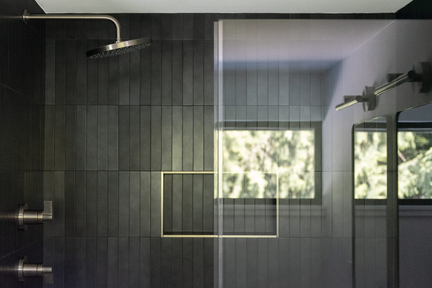 A walk-in shower lined in stacked black tile with a window and a recessed niche