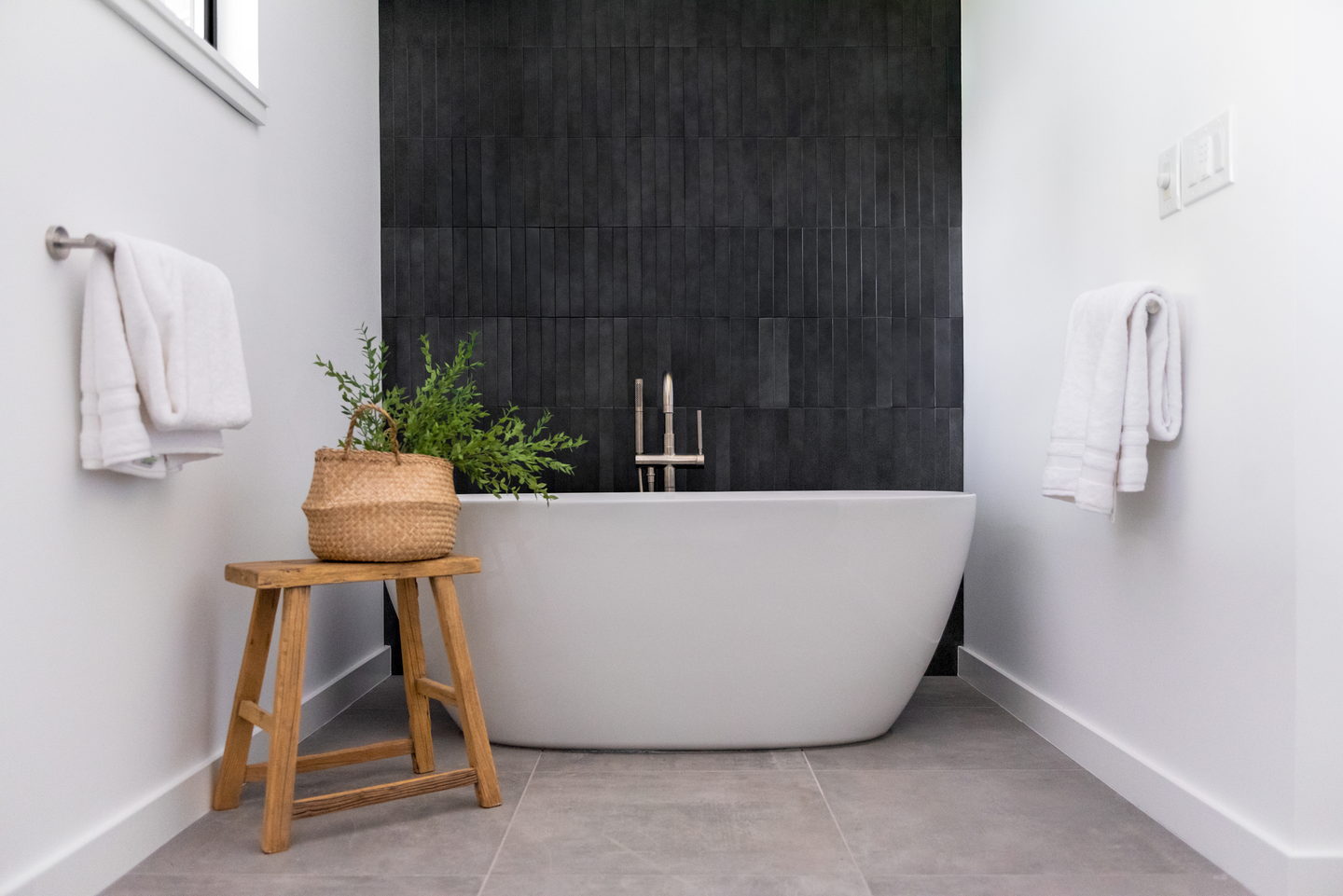 A bathroom with a wall of stacked black tile and a freestanding white tub