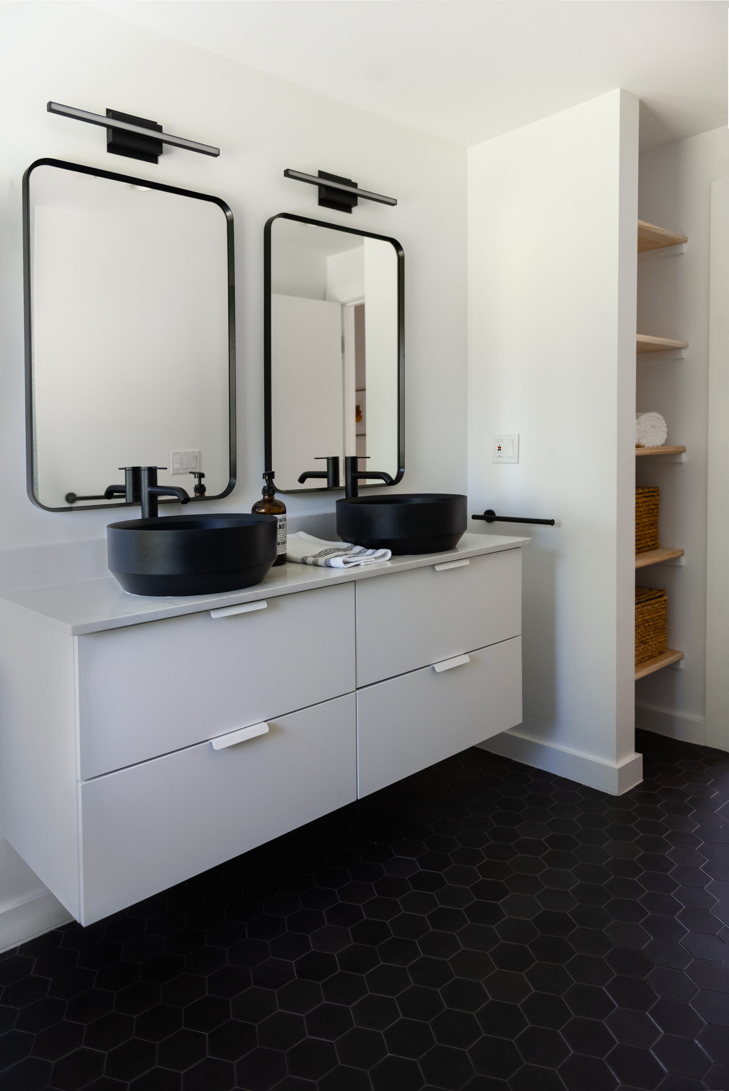 A floating white vanity with two black sinks and two black framed mirrors
