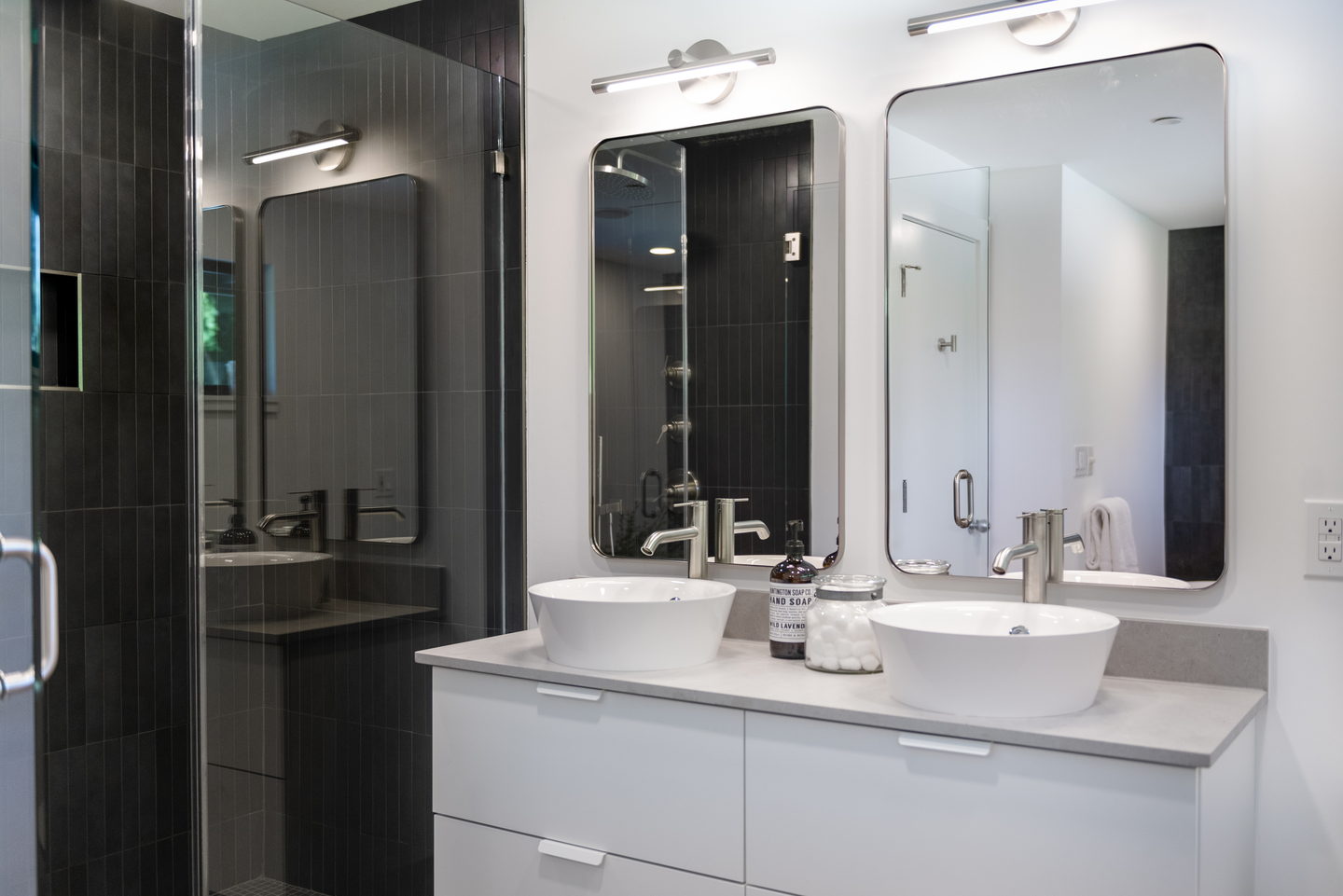 The black tile shower and the white vanity with two sinks and framed mirrors
