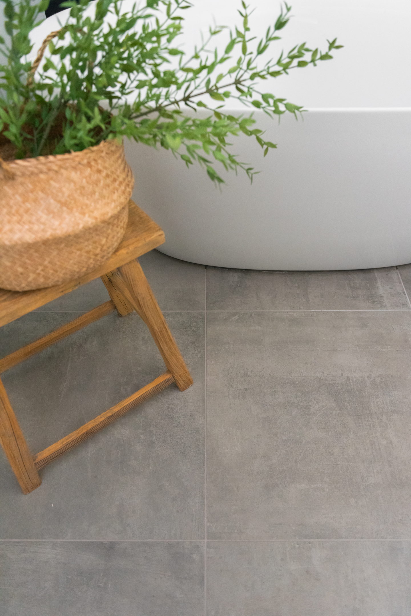 The freestanding tub with a wood stool and a plant on the gray floor