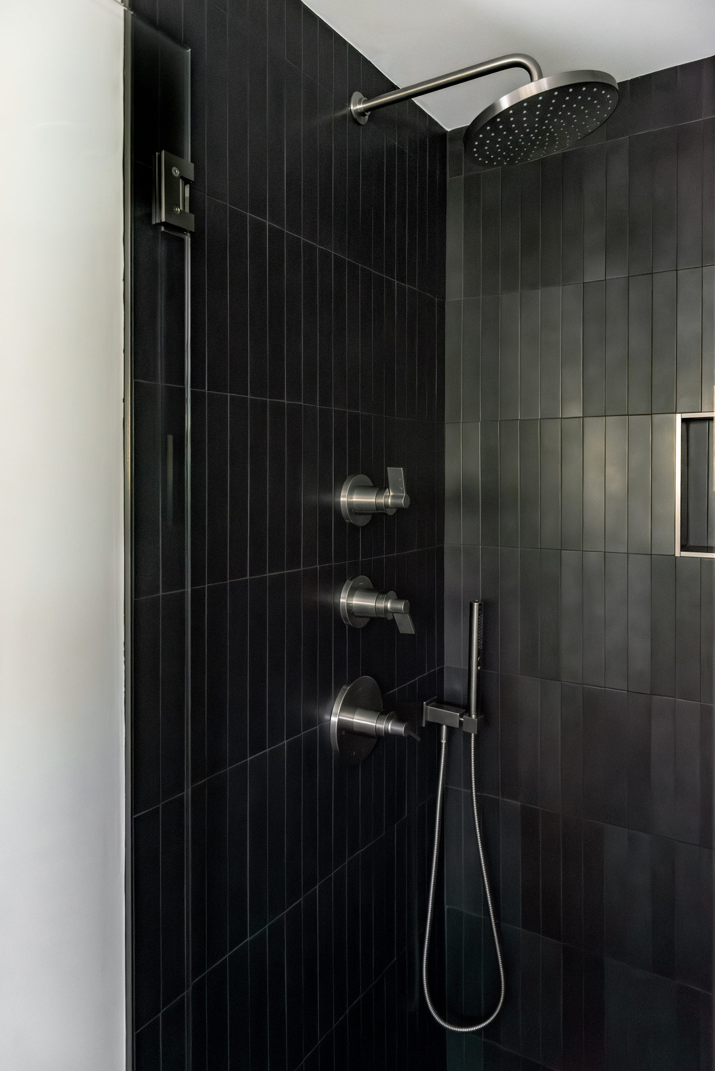 The shower controls and rain head against stacked black tile