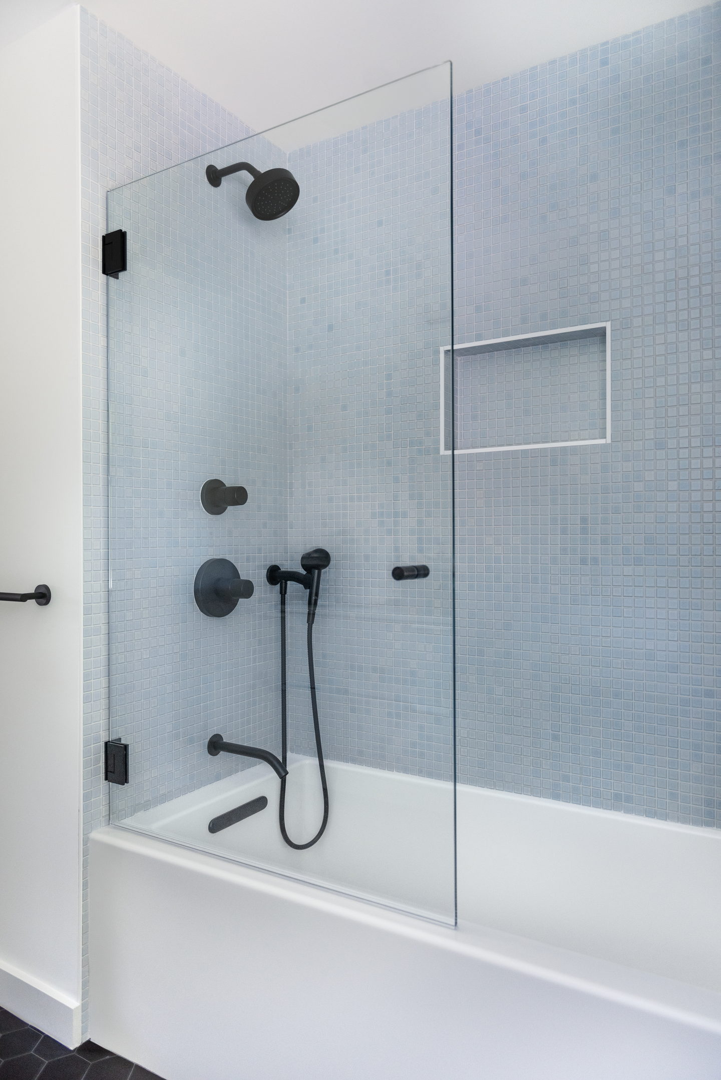 The second bathroom, in pale tile with black fittings and a bath screen