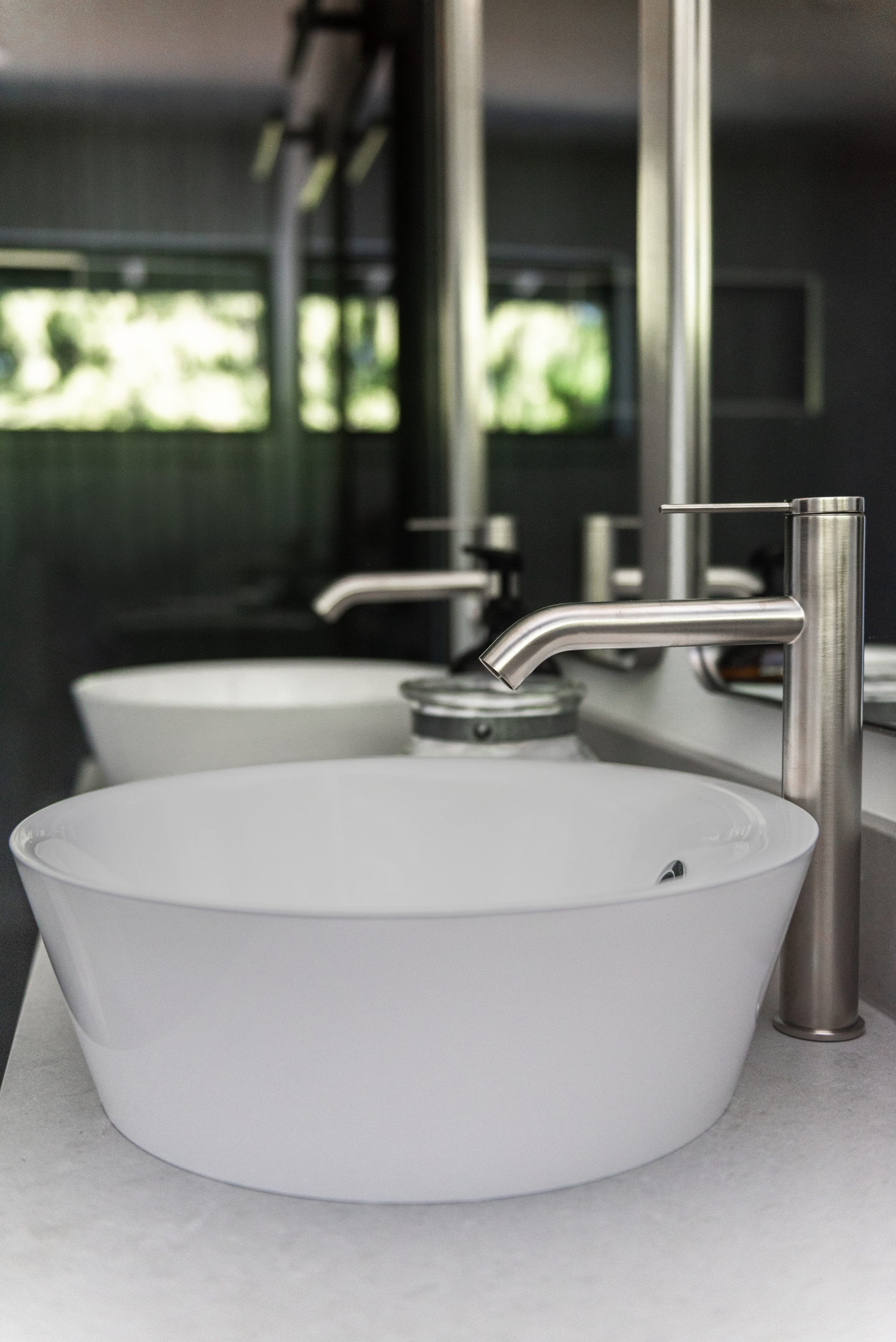 A white sink with a tall stainless faucet against the dark tile