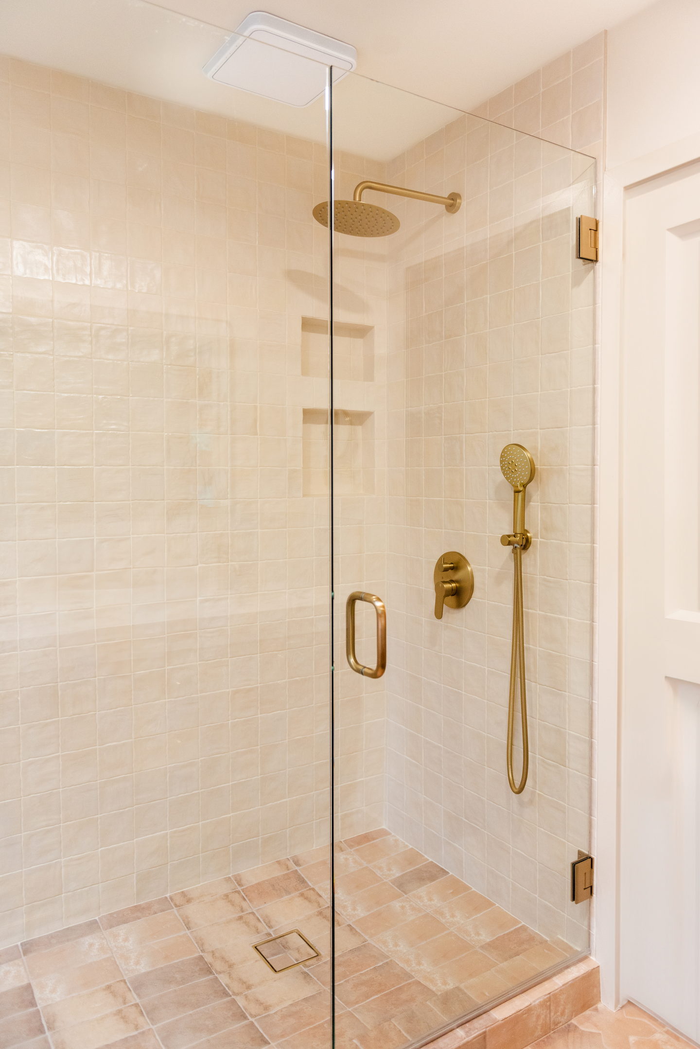 A shower lined in warm limestone with brass fittings and a glass door