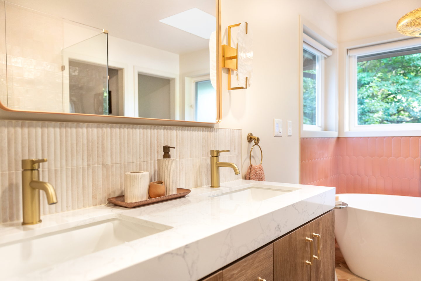A wood vanity with a stone top, brass faucets and a long mirror