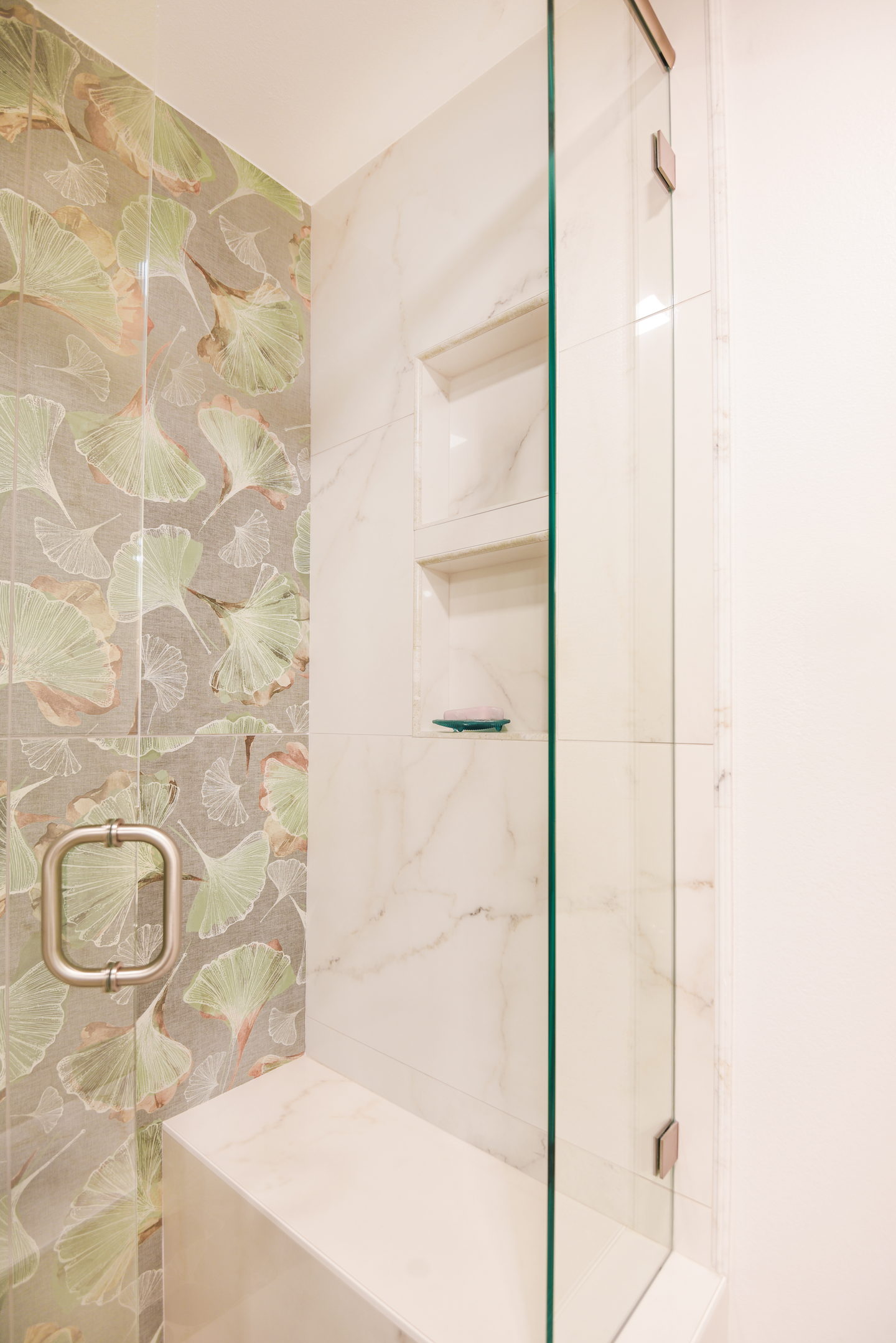 A shower lined in green glass tile with a brass handle on the glass door