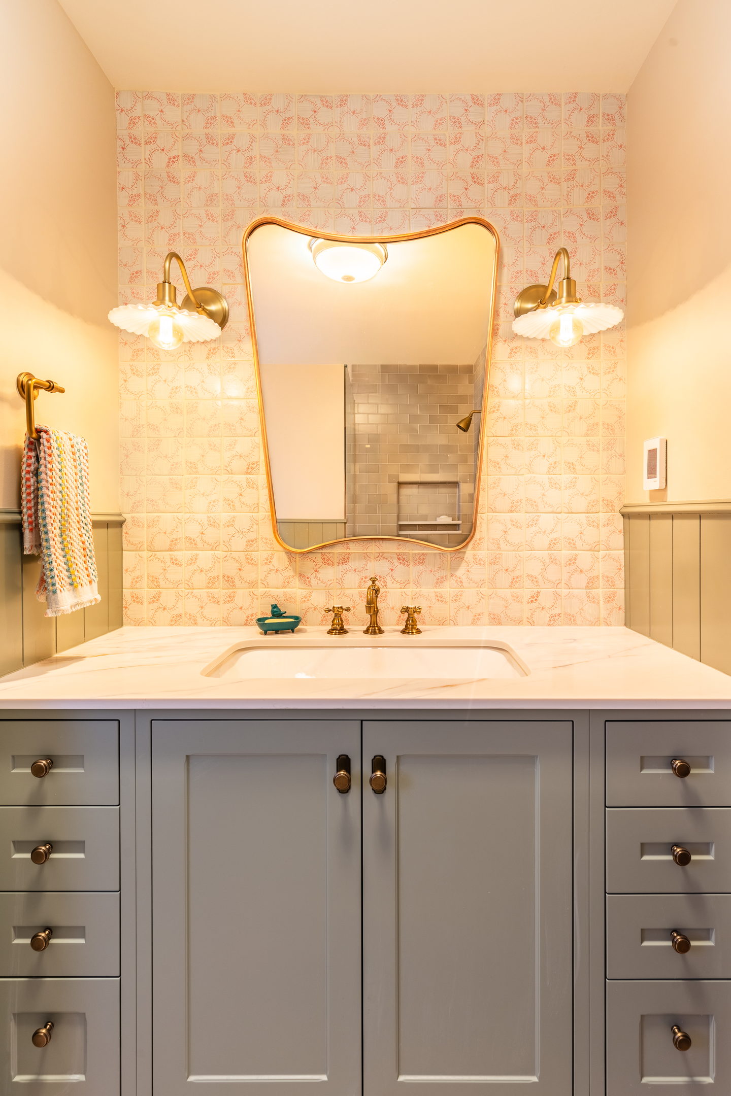 A bathroom with a shaped mirror, wall lights and a gray vanity
