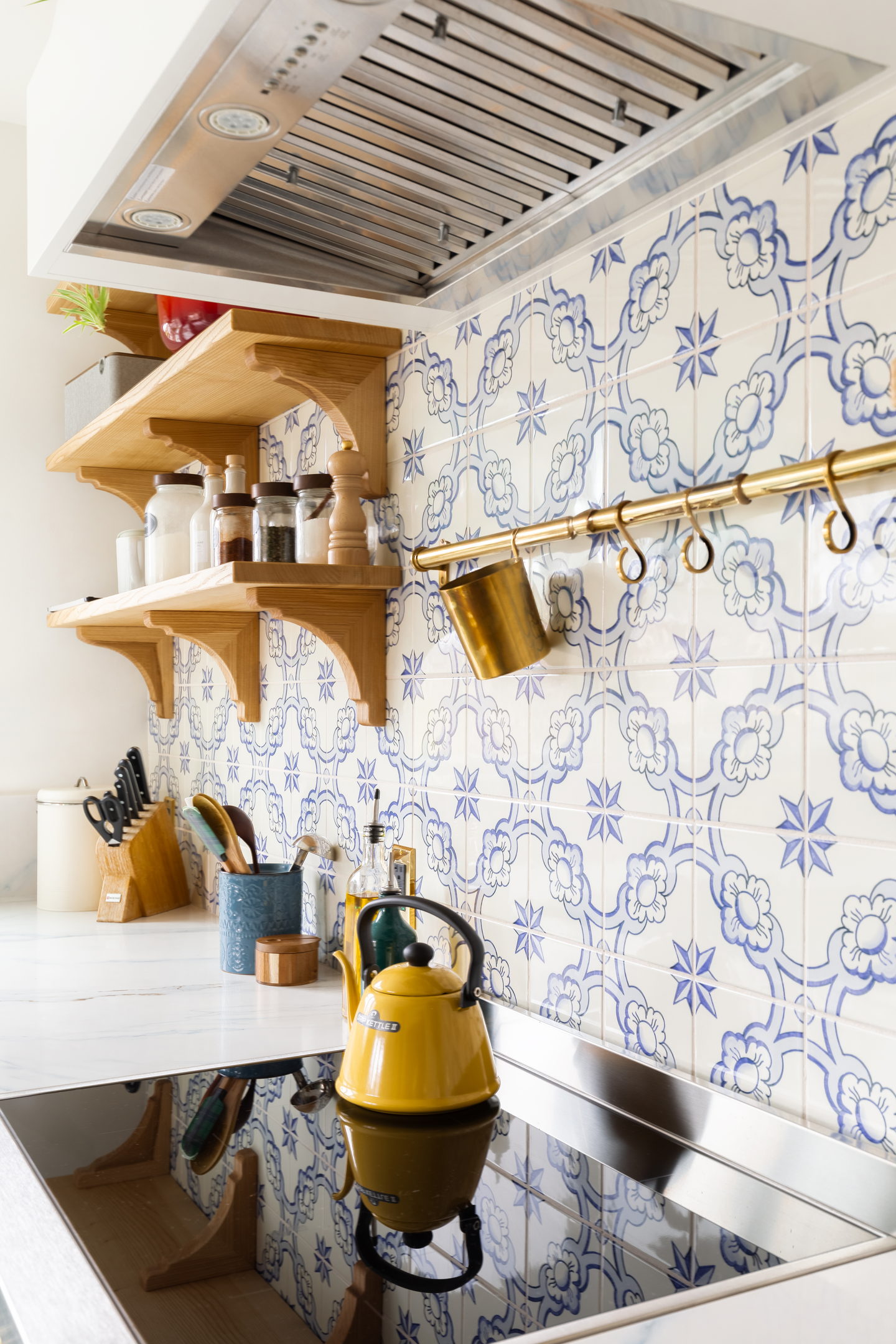 Blue and white patterned tile behind a range with a wood shelf and brass rail
