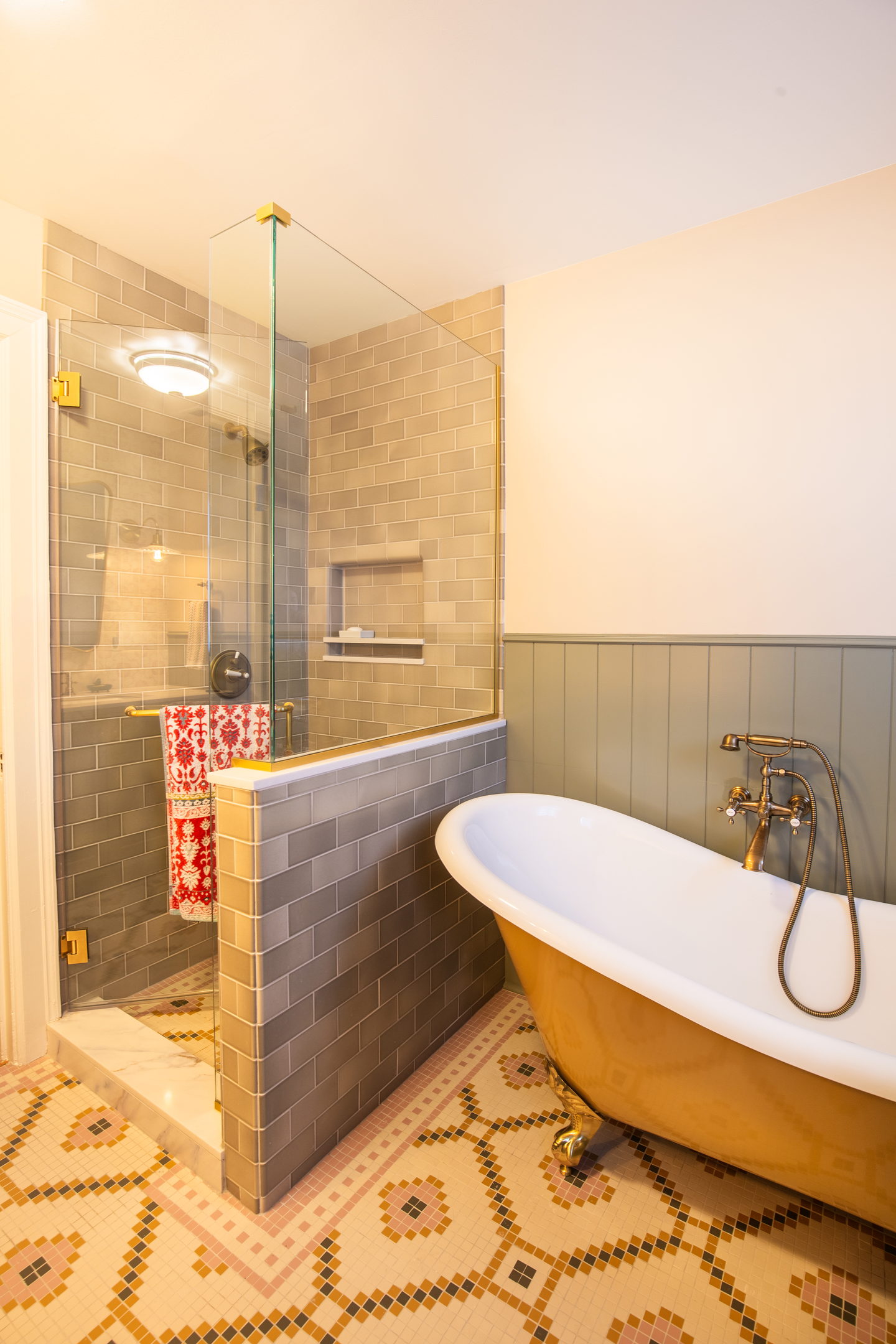 A copper roll-top bath on a patterned tiled floor beside a tiled shower