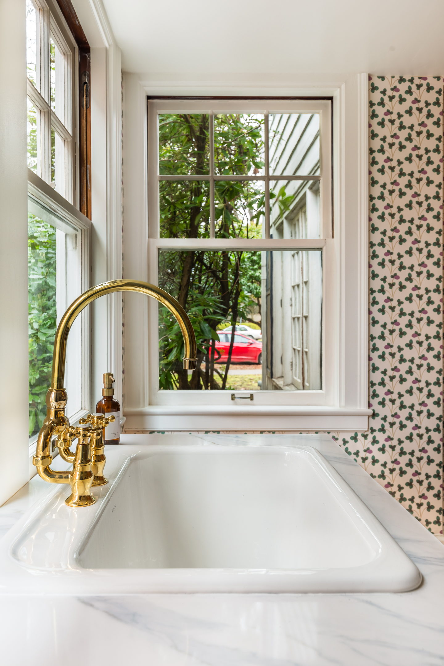 A marble surround and brass bridge faucet at a bathroom window