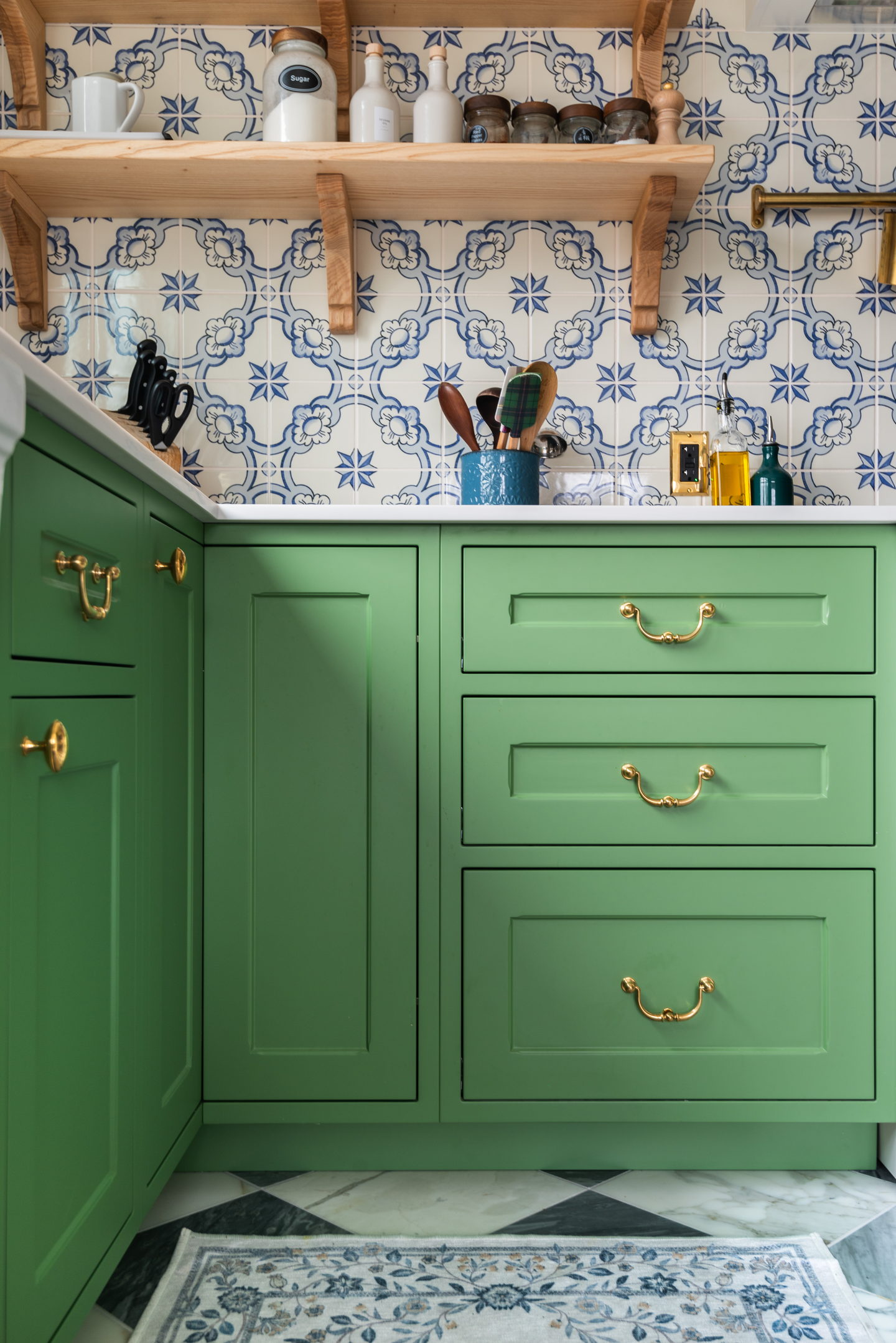 A green painted dresser with brass pulls under patterned tile and open shelves