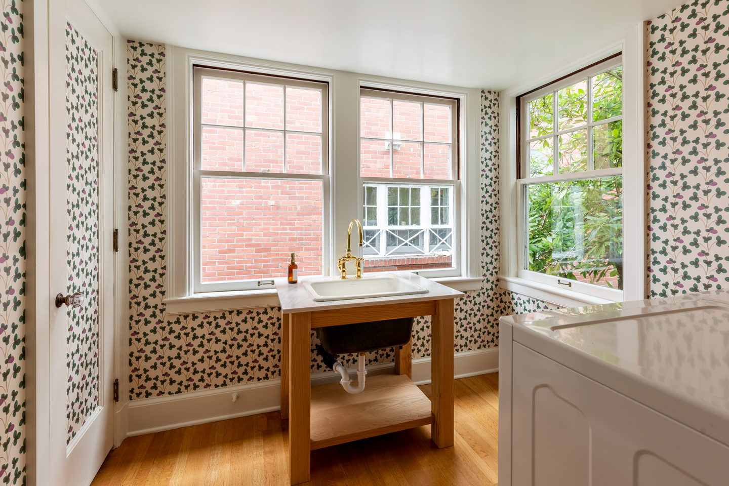 A papered bathroom with a wood washstand between two windows