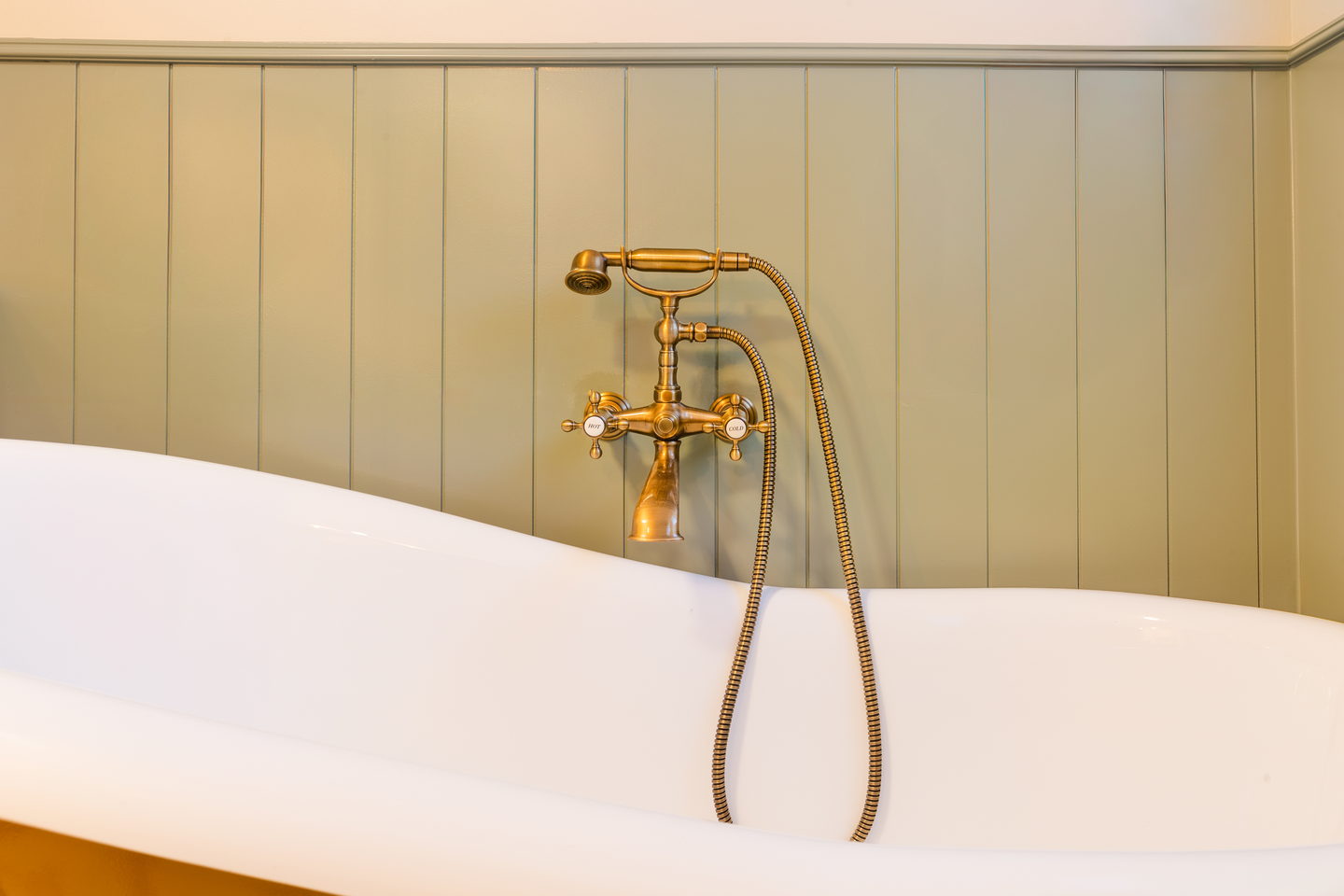 A freestanding tub against pale paneling with a brass floor-standing faucet