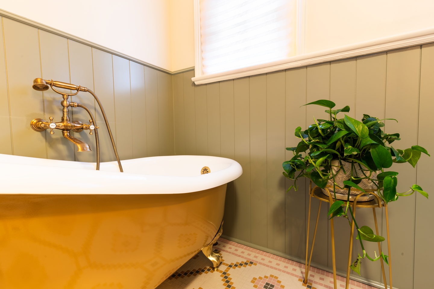 A copper roll-top bath on a patterned floor beside a plant