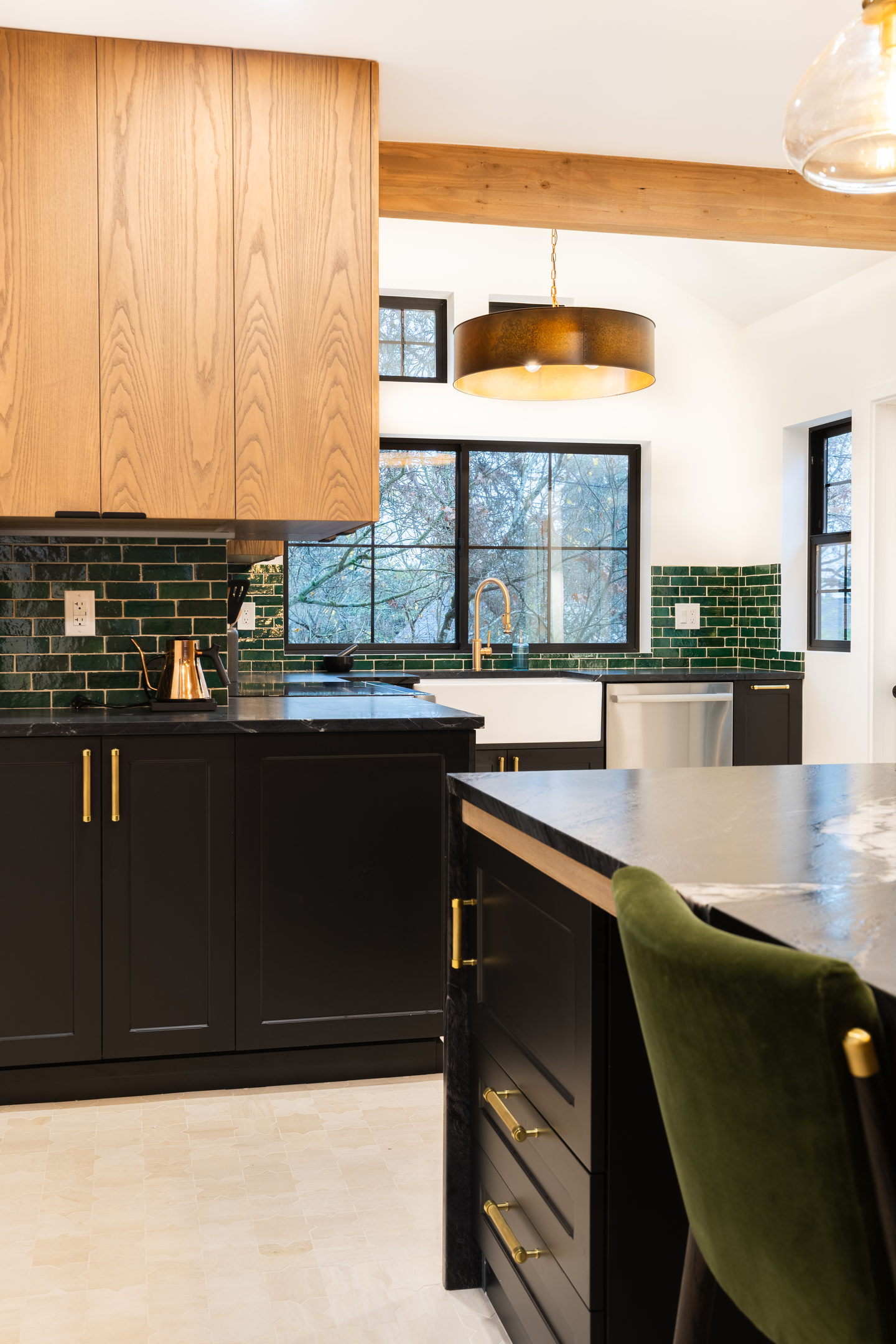 A kitchen with white oak cabinetry, a black island and green tile