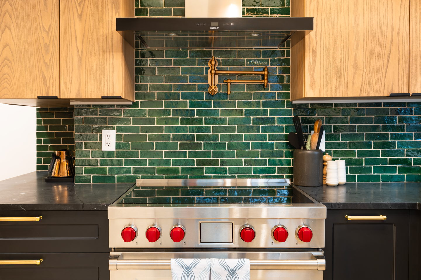 Green zellige tile laid to the ceiling behind a stainless range with a brass pot filler